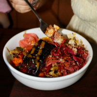 Colorful poke bowl with tuna, rice, seaweed, and vegetables, being picked up with chopsticks.