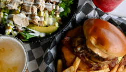 A cheeseburger with fries and a side salad on a checkered table, with a glass of beer nearby.