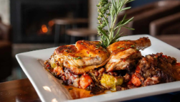 Roasted chicken pieces with crispy skin on a bed of vegetables, garnished with rosemary, on a white plate.