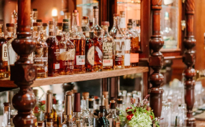 Bar interior with a wide variety of liquor bottles on wooden shelves and warm lighting.