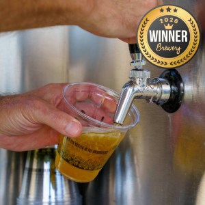 Pouring beer from a tap into a plastic cup, with a gold award badge reading 'Winner Brewer 2026' in the top right corner.