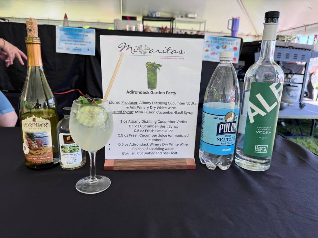 Bar setup with a margarita-style cocktail in the foreground, bottles on either side, and a printed menu that reads Adirondack Garden Party.