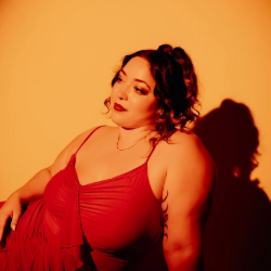 Woman in a red dress lounges against an orange backdrop, gazing to her left with a confident expression.
